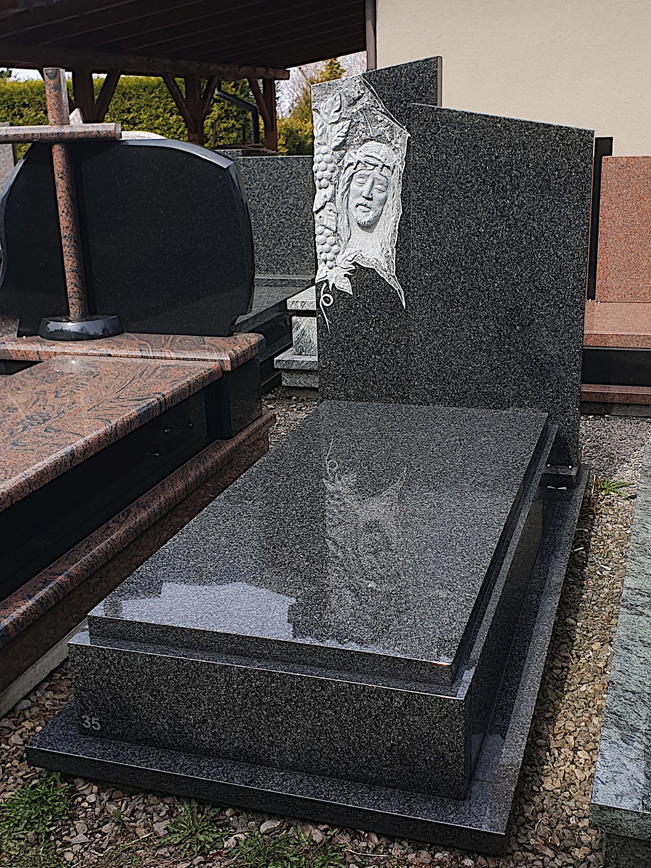 Nowoczesny nagrobek pojedynczy z granitu "Impala" z ręcznie wykonaną płaskorzeźbą Jezusa w koronie cierniowej oraz asymetryczną tablicą