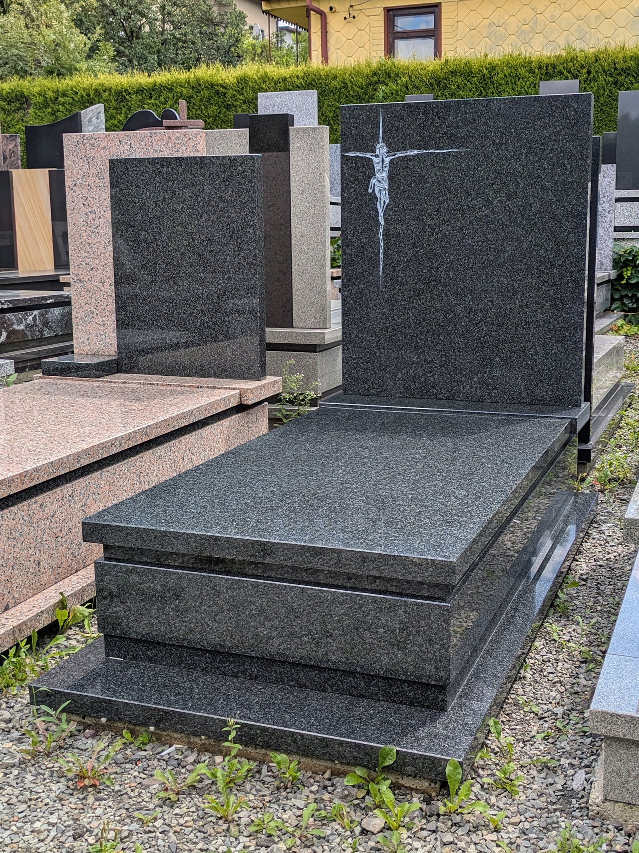 Prosty nagrobek pojedynczy z granitu "Impala" z minimalistyczną płąskorzeźbą Jezusa na krzyżu i wykończeniem w kantach